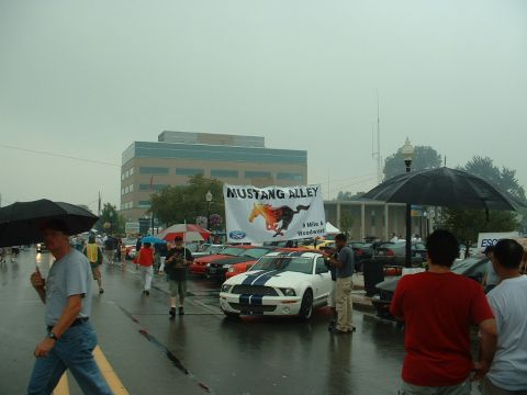 1978 Ford Mustang II - Cars gather for the Mustang Alley event on a wet day, with a banner overhead.