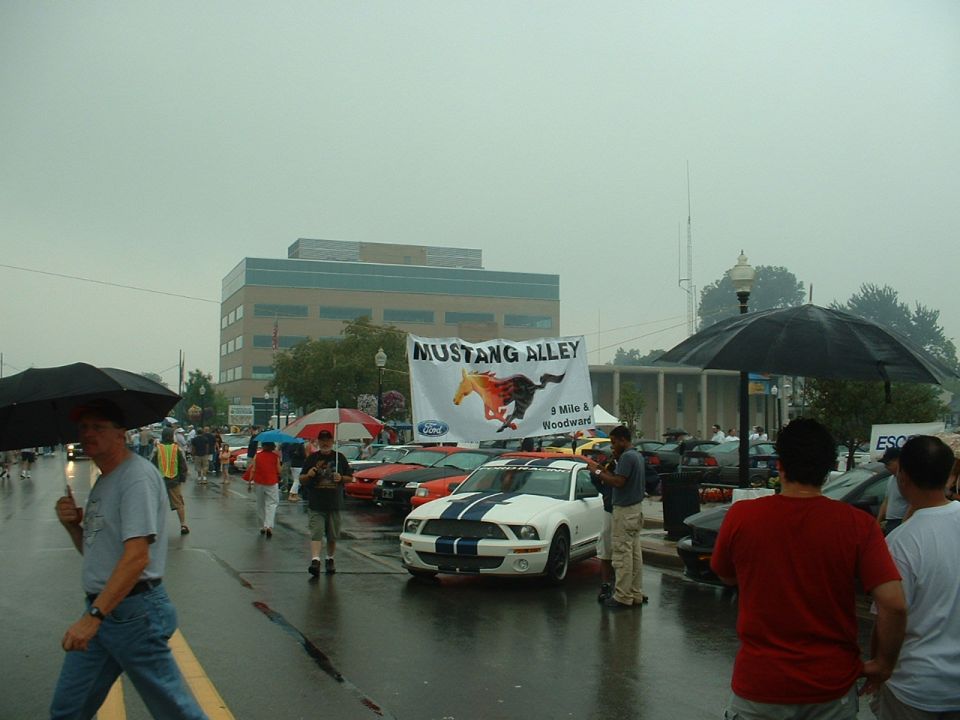 White Ford Mustang with blue stripes at Mustang Alley event, rainy day