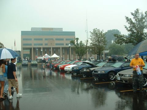 1978 Ford Mustang II - A car show is underway on a rainy day, with several Ford Mustangs on display.