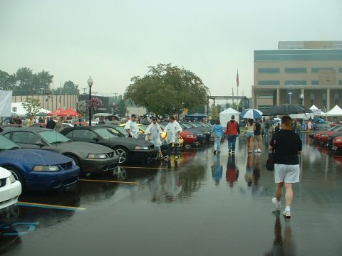 1978 Ford Mustang II - A line of Ford Mustangs are parked on a wet lot during an outdoor event.