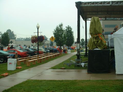 1978 Ford Mustang II - An outdoor event features rows of parked cars, a stage, and a covered display under a cloudy sky.