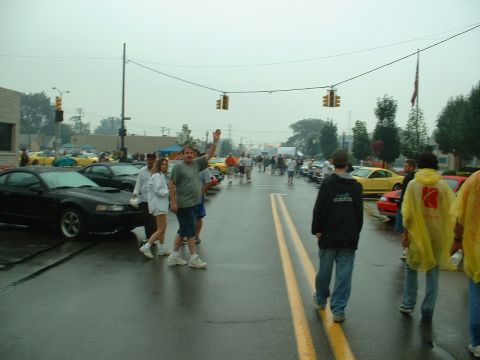 1978 Ford Mustang II - A black Ford Mustang is parked on a wet street during a car show with people walking around.