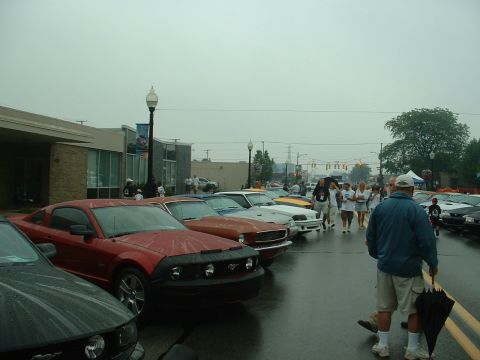1978 Ford Mustang II - Several Ford Mustangs are parked on a wet street during an outdoor car show.
