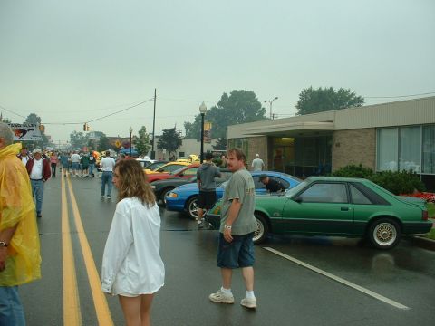 1978 Ford Mustang II - A green coupe is parked on a street during a car show event with many people around.