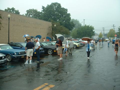 1978 Ford Mustang II - A gathering of Ford Mustangs in the rain outside a public library.