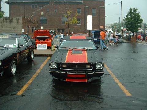 1978 Ford Mustang II - Front view of a black Mustang II Cobra with red and orange hood and front-spoiler stripes, snake grille emblem, hood scoop and quad round h…