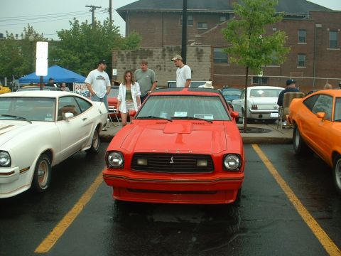 1978 Ford Mustang II - Front view of a red Mustang II hatchback with hood louvers, a front air dam, gold pinstriping and a FORD-lettered running-pony grille, park…
