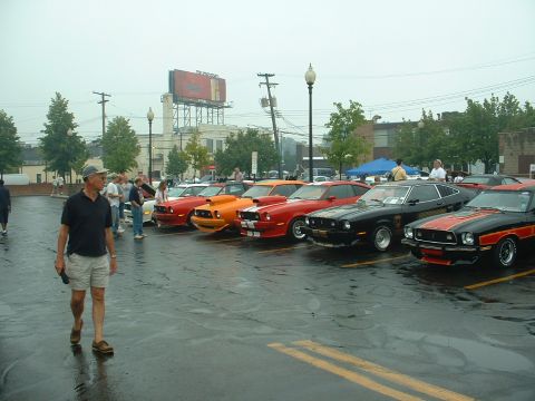 1978 Ford Mustang II - A line of classic Ford Mustang IIs are parked in a lot, with a man walking in the foreground.