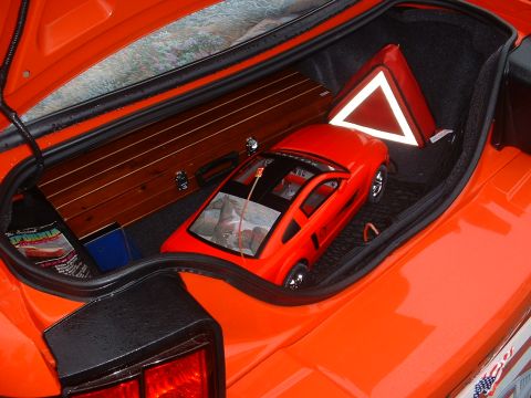 1978 Ford Mustang II - Trunk of a car holding a red toy Mustang, a wooden panel, and a reflective triangle safety sign.