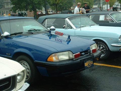 1978 Ford Mustang II - A blue police car, likely a 1987 Ford Mustang GT, is parked next to other vehicles at an outdoor event.