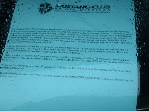 1978 Ford Mustang II - A document detailing the restoration of a 1992 Michigan State Police Mustang patrol car is visible through a window with water droplets.