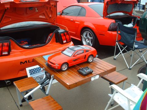 1978 Ford Mustang II - Two orange Ford Mustangs are displayed, one with a remote-controlled model on a picnic table.