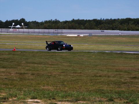 2001 Mercury Grand Marquis - A black Porsche 911 with a distinctive rear spoiler drives on a race track under a clear blue sky.
