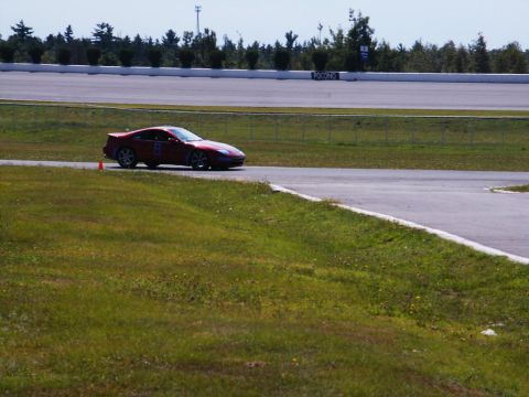 2001 Mercury Grand Marquis - A red sports car navigates a turn on a paved race track with grassy verges.