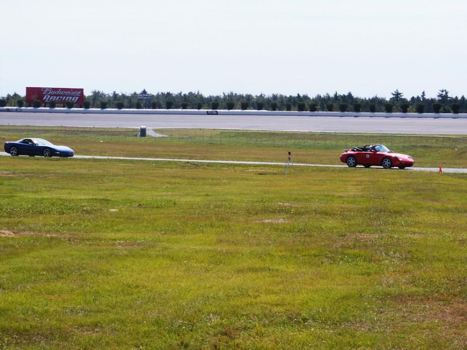 Blue sports car and red convertible on a racetrack with a Budweiser Racing billboard in the background