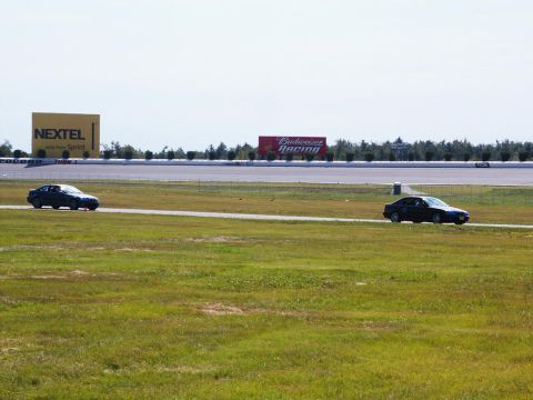 2001 Mercury Grand Marquis - Two cars race on a track with large billboards visible in the distance.