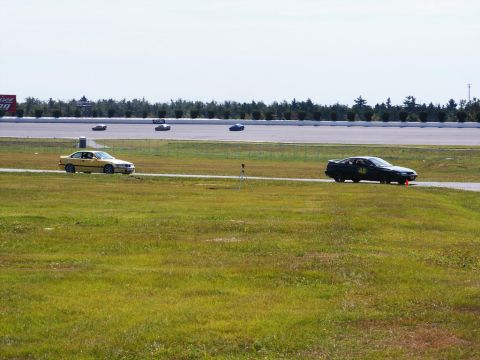 2001 Mercury Grand Marquis - Multiple cars compete on a sunny day at a racetrack with grassy infield.