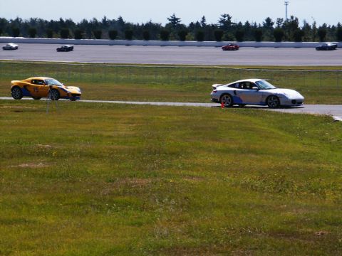 2001 Mercury Grand Marquis - A silver Porsche 911 and a yellow Lotus race on a track, with other cars in the distance.