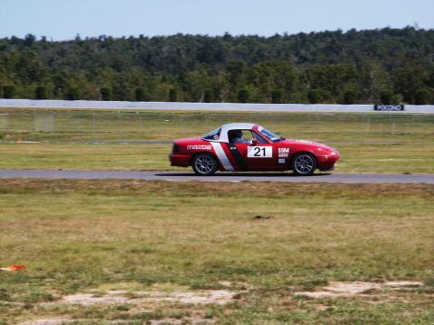 2001 Mercury Grand Marquis - A red Mazda Miata with racing decals is seen on a race track.