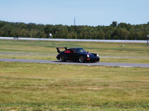 2001 Mercury Grand Marquis - A black Porsche 911 with a prominent rear wing speeds around a race track on a sunny day.