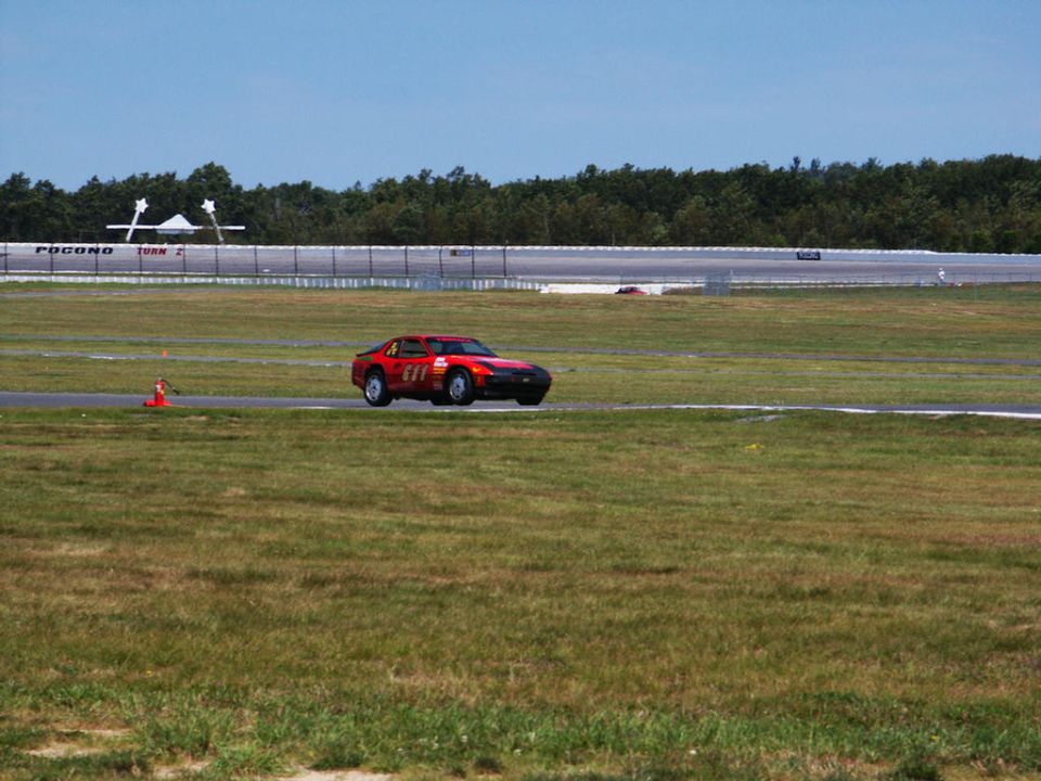 Red race car with number 611 on the side, driving on a race track with a grandstand in the background