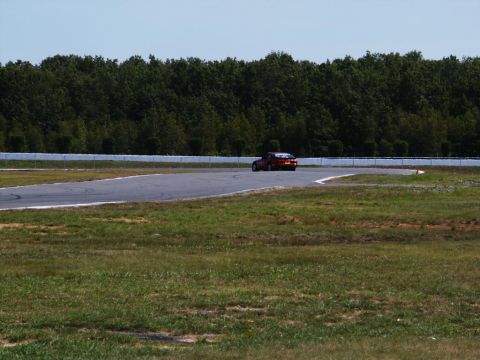 2001 Mercury Grand Marquis - A red car drives on a race track with trees in the background.