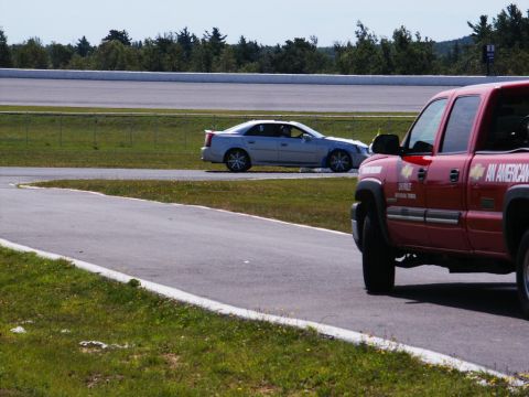 2001 Mercury Grand Marquis - A silver sedan is seen on a race track, with a red truck partially visible in the foreground.