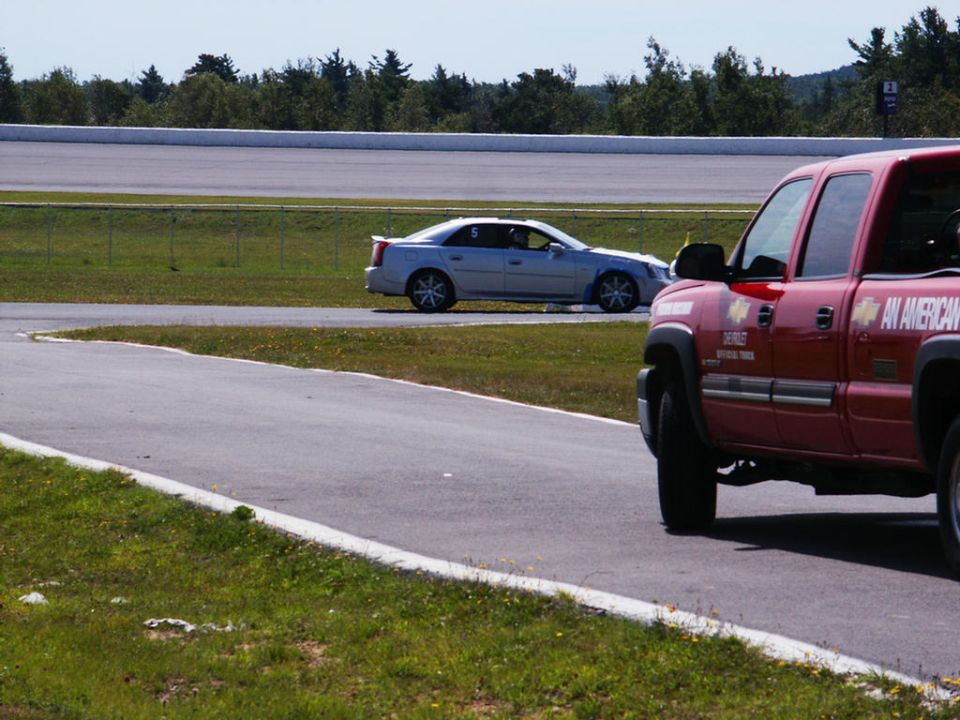 Silver sedan on race track, side view. Red truck in foreground