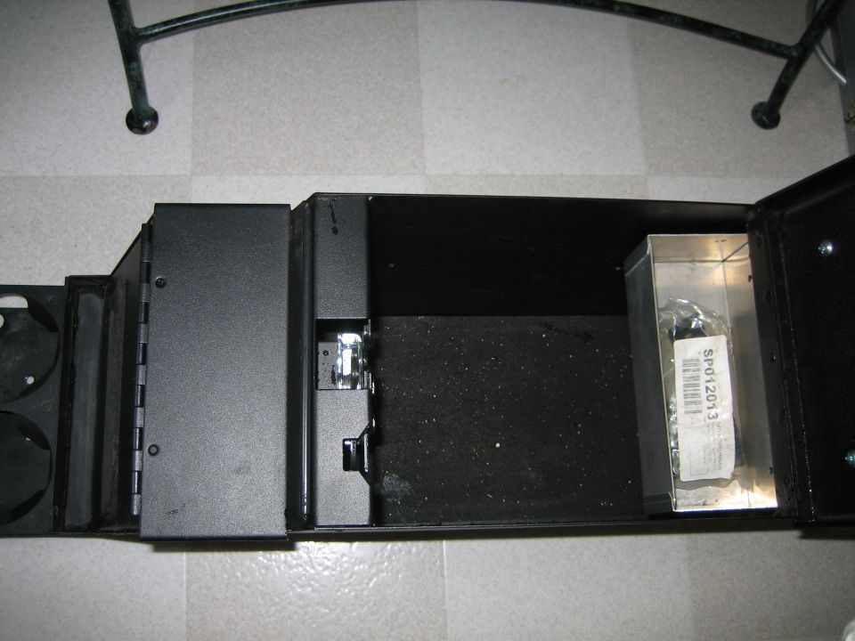 Center console storage compartment with a small metal box containing a part labeled SP012013