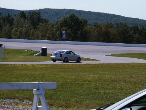 2001 Mercury Grand Marquis - A silver Cadillac CTS drives around a turn on a race track with trees and hills in the background.