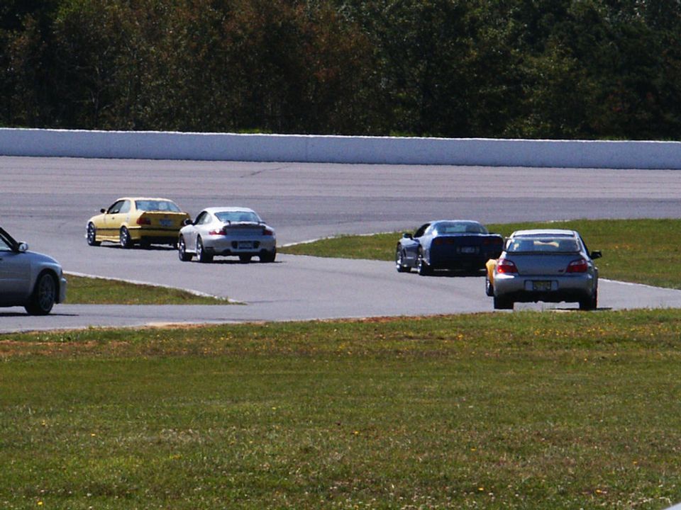 Several cars are racing on a track, including a yellow BMW, a silver Porsche, and a dark blue car