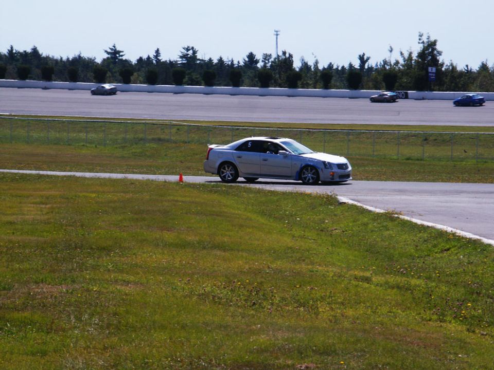 Silver Cadillac CTS-V on a race track, number 5 on door. Other cars in distance