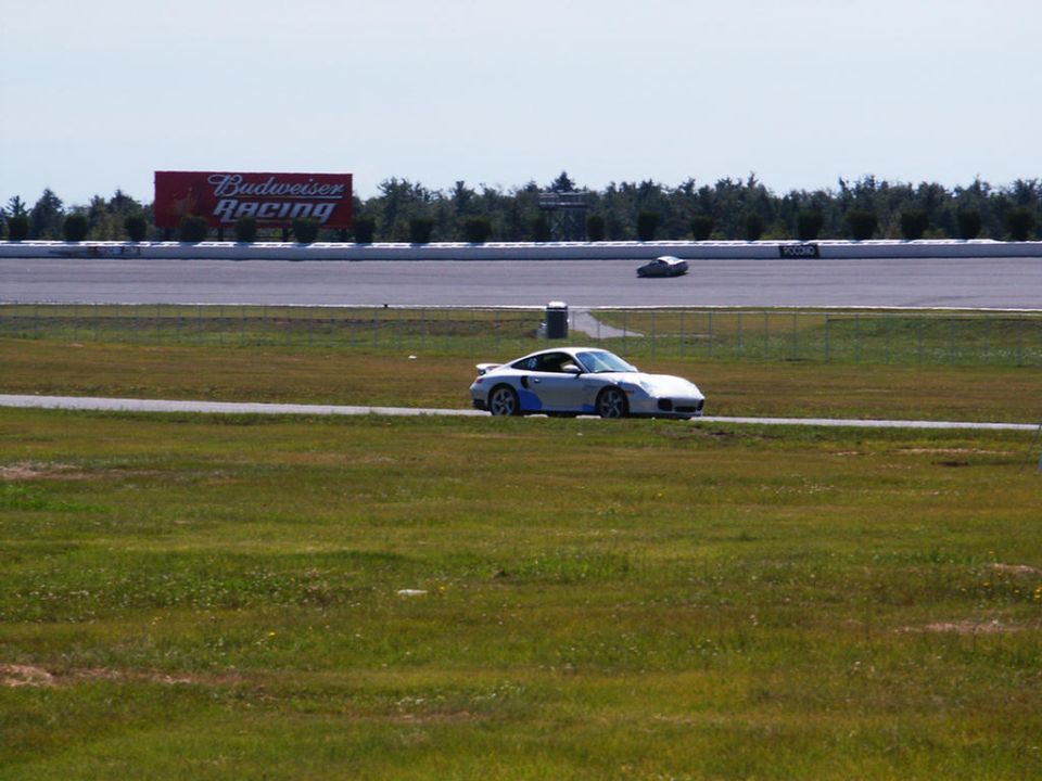 Silver Porsche 911 on a race track with a Budweiser Racing billboard in the background