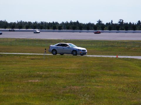 2001 Mercury Grand Marquis - A silver sedan drives on a race track with other vehicles visible in the background under a clear sky.
