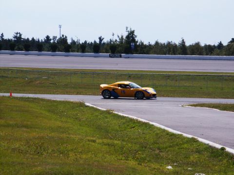 2001 Mercury Grand Marquis - A yellow sports car navigates a turn on a race track under a clear sky.