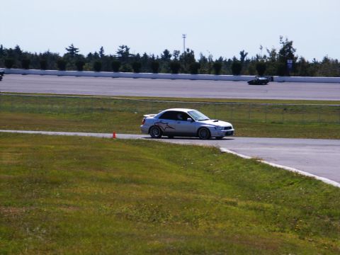2001 Mercury Grand Marquis - A silver Subaru WRX STI navigates a turn on a race track, with another vehicle visible in the distance.