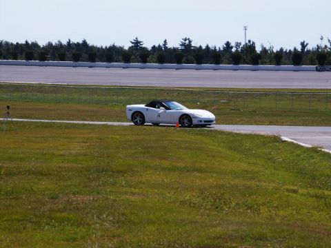 2001 Mercury Grand Marquis - White convertible sports car on a race track with trees and grandstands in the background.