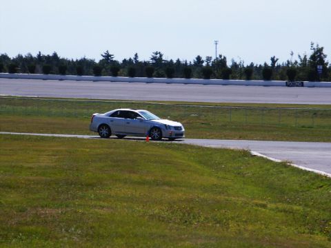 2001 Mercury Grand Marquis - A silver Cadillac CTS is on the track at Pocono Raceway, with trees and a grandstand in the background.