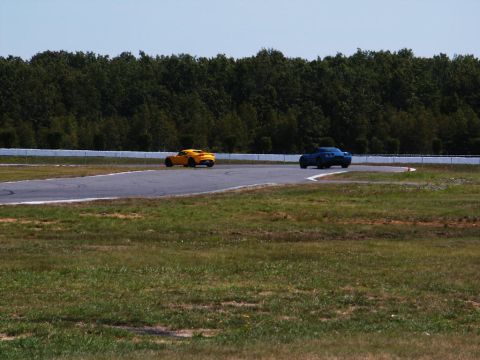 2001 Mercury Grand Marquis - Two sports cars, one yellow and one blue, navigate a turn on a race track under a clear sky.