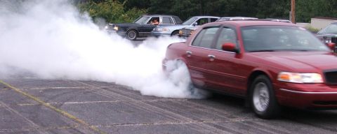1985 Ford LTD Crown Victoria - A dark red Ford Crown Victoria doing a burnout in a paved lot, its rear tires buried in a huge cloud of white tire smoke as it sits on poli…