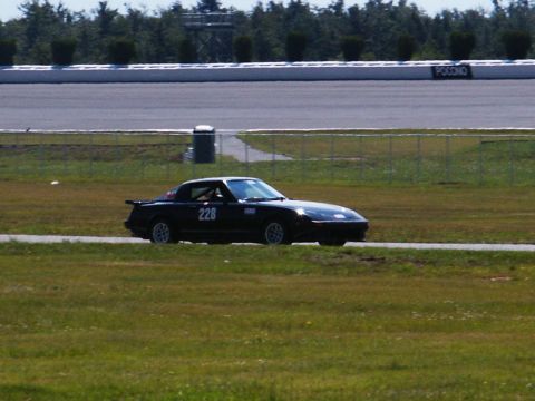 2001 Mercury Grand Marquis - A black sports car with racing numbers drives on a track with trees and a fence in the background.