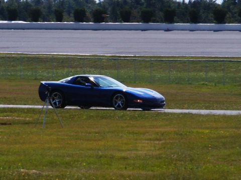 2001 Mercury Grand Marquis - A blue C5 Corvette drives on a paved track with grassy infield.