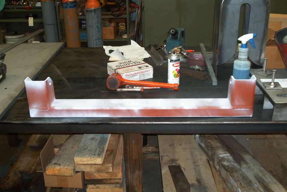 Red and white painted metal crossmember part on a workbench with tools
