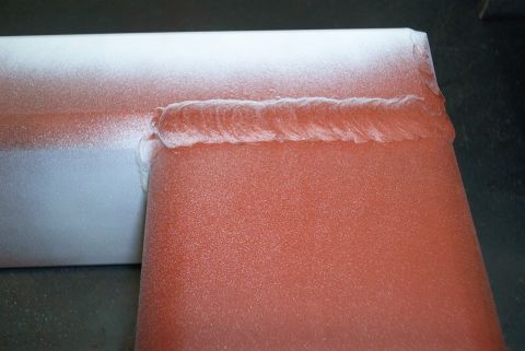1983 Ford Bronco - Close-up of a welded metal component, painted with orange and white spray paint, revealing a coarse weld bead.