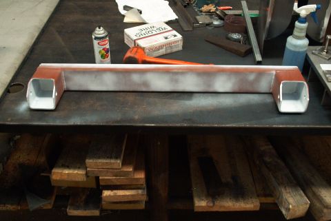 1983 Ford Bronco - A metal crossmember part is shown with red and white primer, along with a can of spray paint and a box of welding wire.