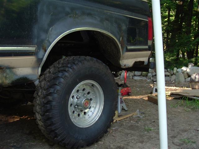 Black and tan Ford Bronco rear quarter panel with large off-road tire, showing rust and damage