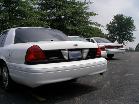 2001 Ford Crown Victoria - Two white Ford Crown Victorias are parked side-by-side in an outdoor lot.