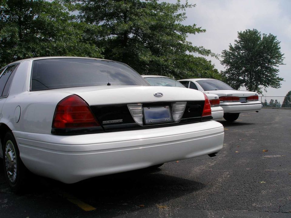 Rear view of two white Ford Crown Victorias parked in a lot
