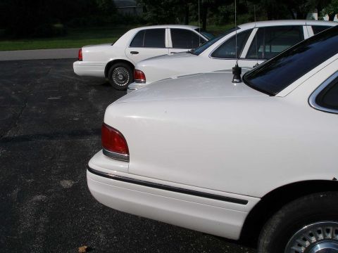 2001 Ford Crown Victoria - Two white sedans, likely Ford Crown Victorias, are parked side-by-side in a lot.