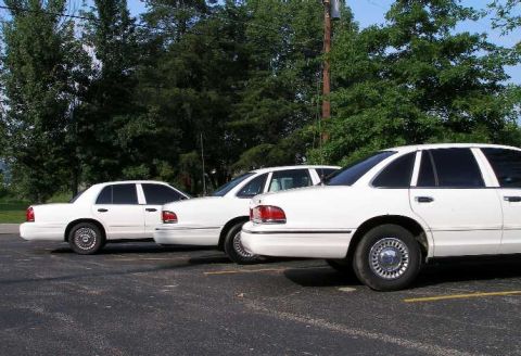 2001 Ford Crown Victoria - Three white Ford Crown Victorias are parked in a lot on a sunny day.